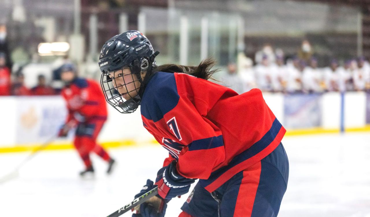 A female athlete skates in full equipment on the ice during a hockey game.