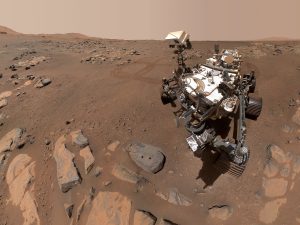 The Mars Perseverance rover on the surface of Mars, a red dusty looking terrain.