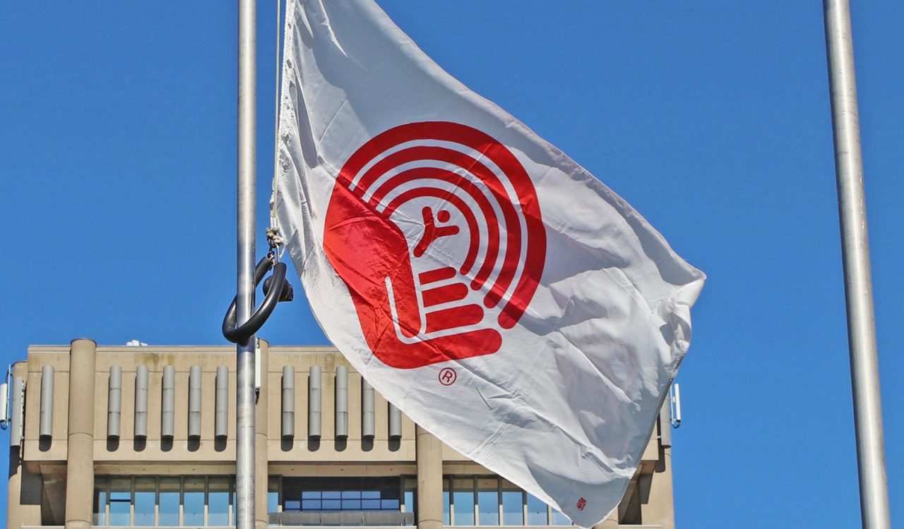 A closeup image of the United Way flag flying on a pole in front of Brock University’s Schmon Tower.