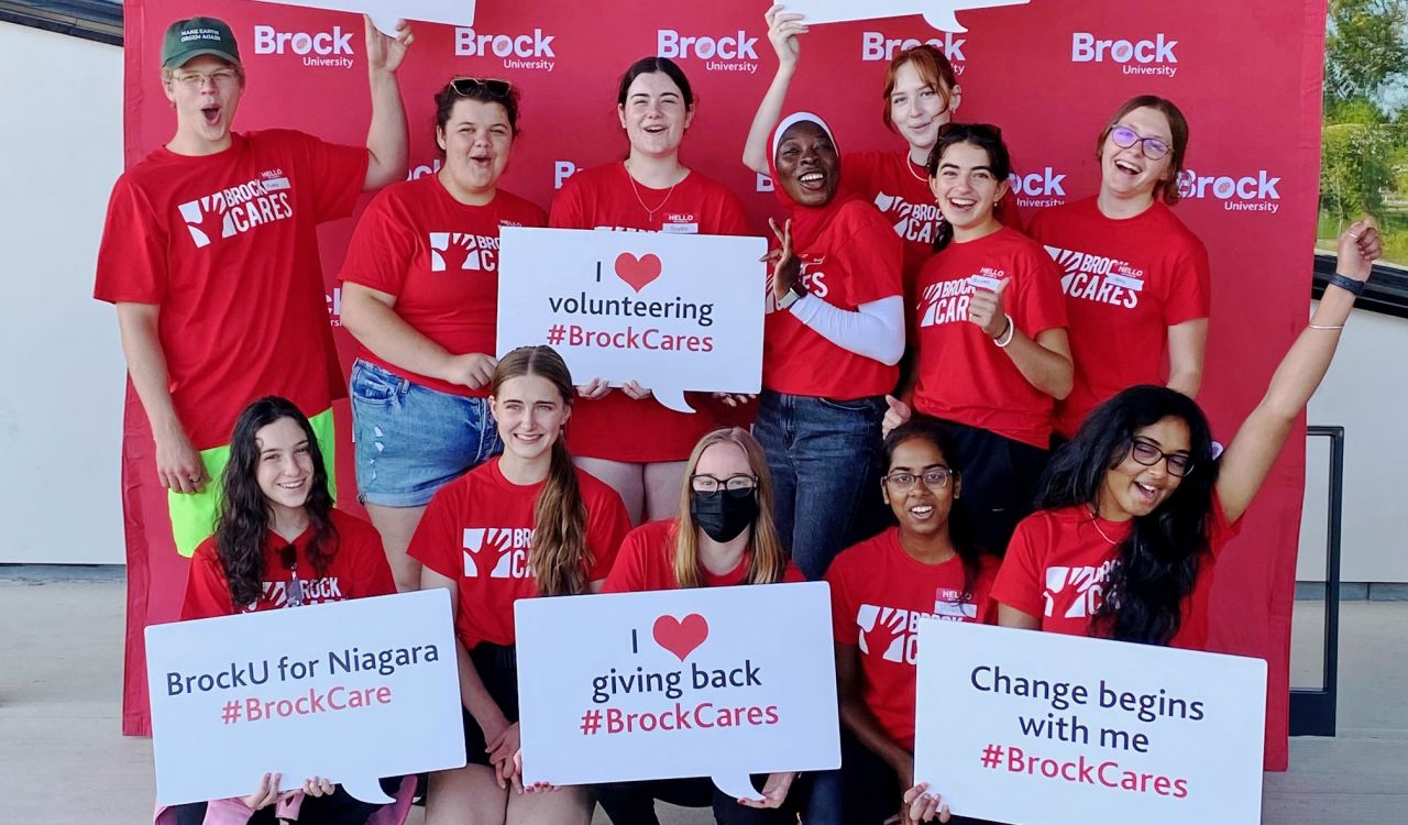 A group of students wearing Brock Cares shirts stand with signs that talk about their care for the community.