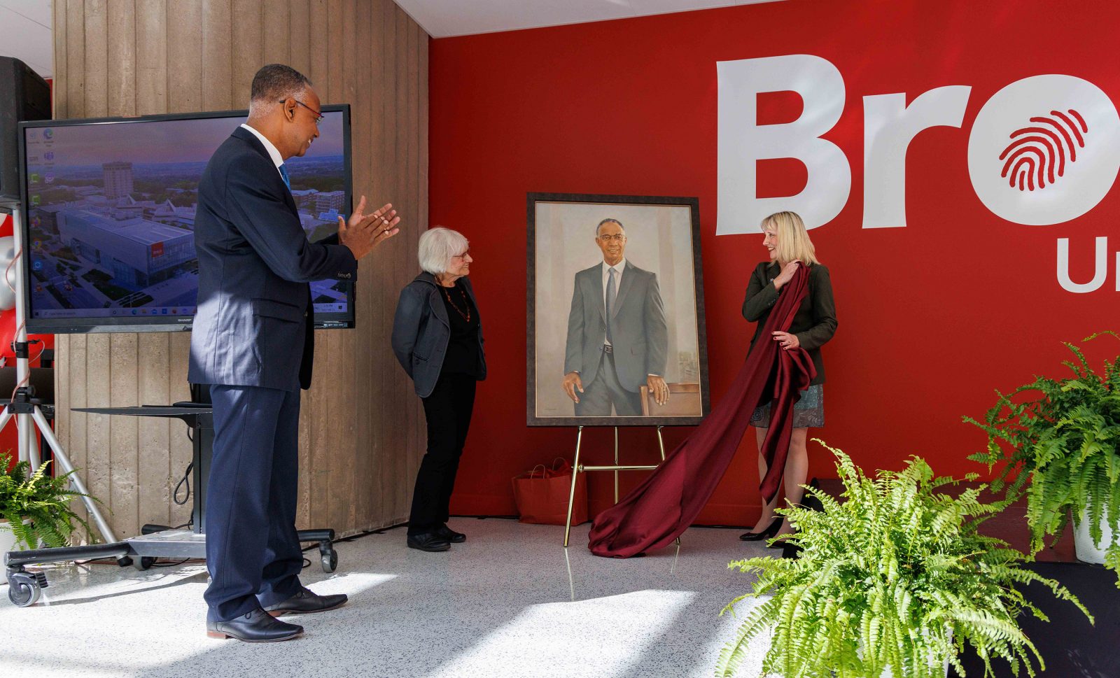 Three people unveil a painted portrait.
