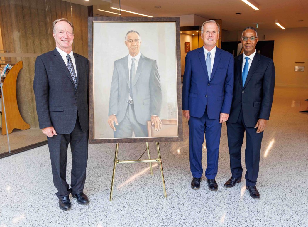 Three men stand with a painted portrait.