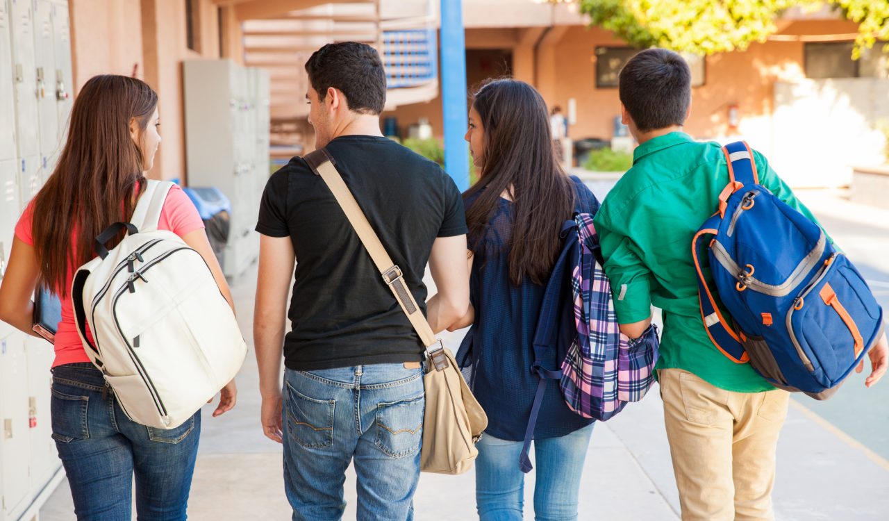 Four high school students walk together outside along rows of lockers