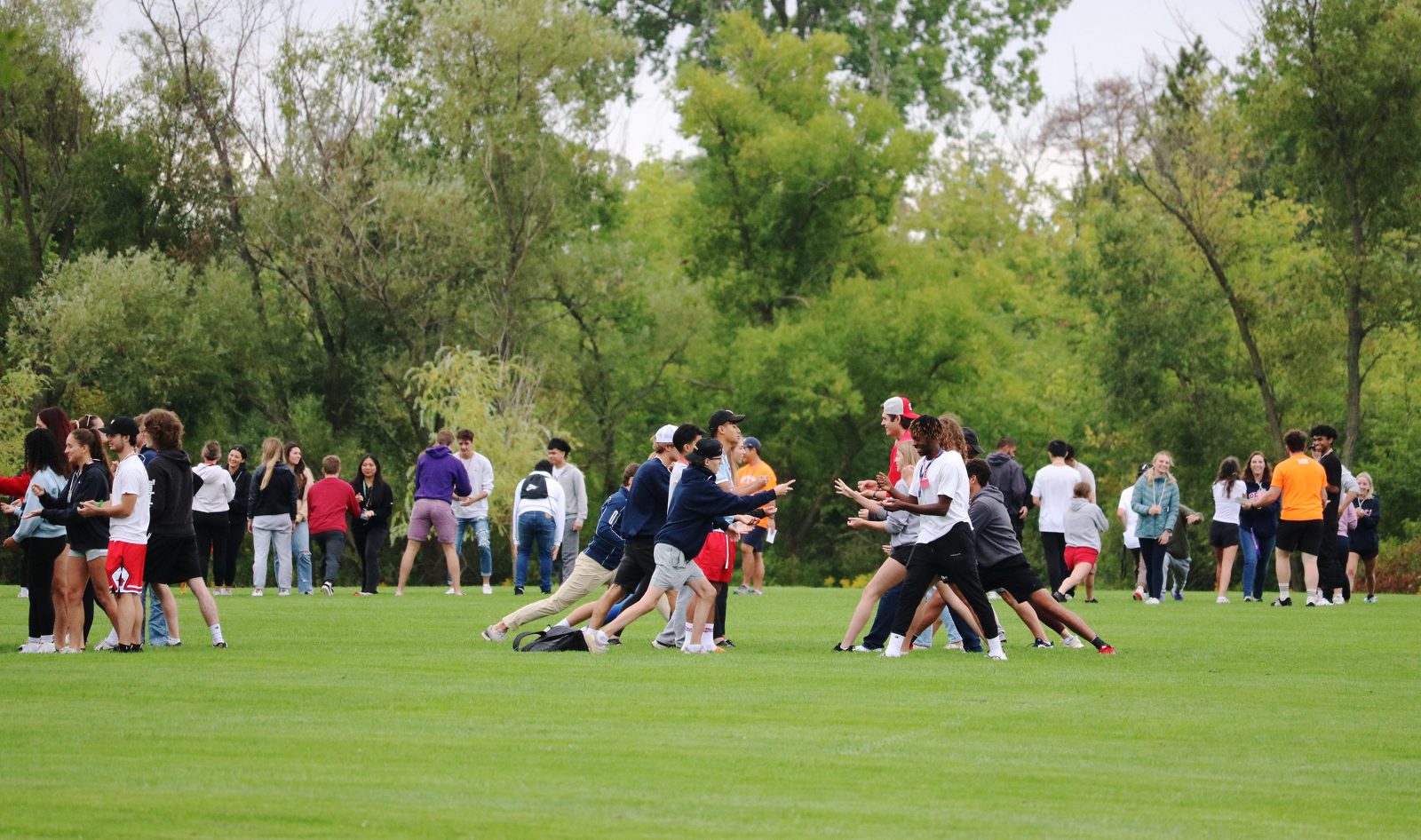 A group of people play rock, paper, scissors on a green field while facing one another.