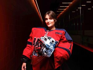A woman stands in a hallway holding a hockey helmet.