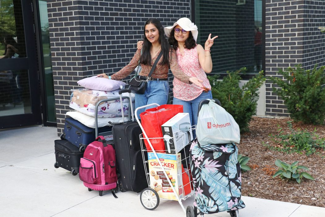 A woman and her mother stand together smiling behind a pile of luggage.