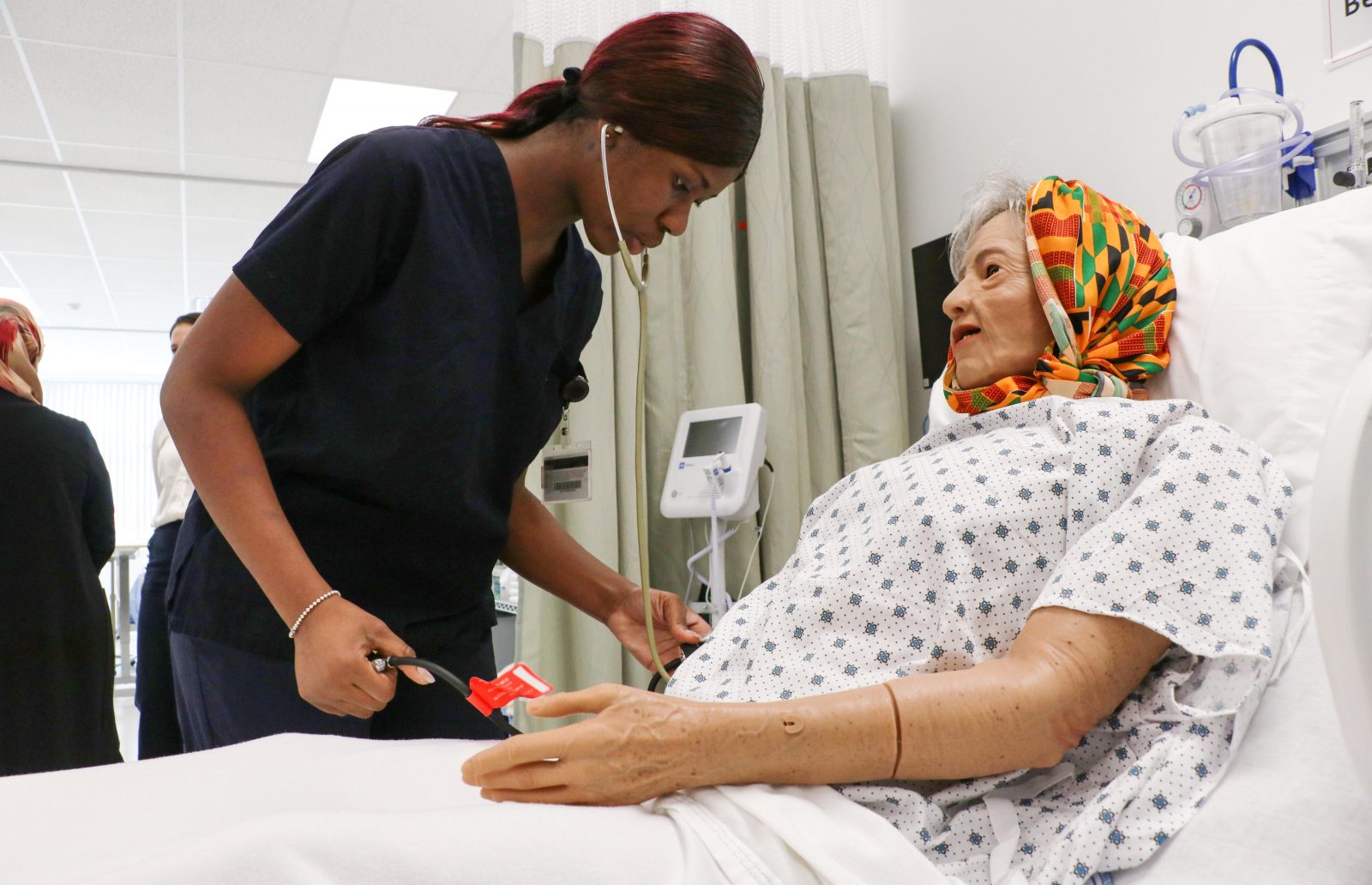 A nurse examines a patient simulator in a nursing lab designed to look like a hospital room.