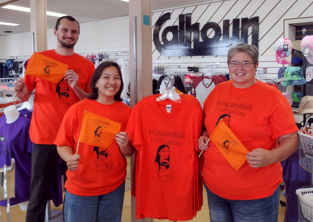 Three people wearing orange shirts stand in a store.