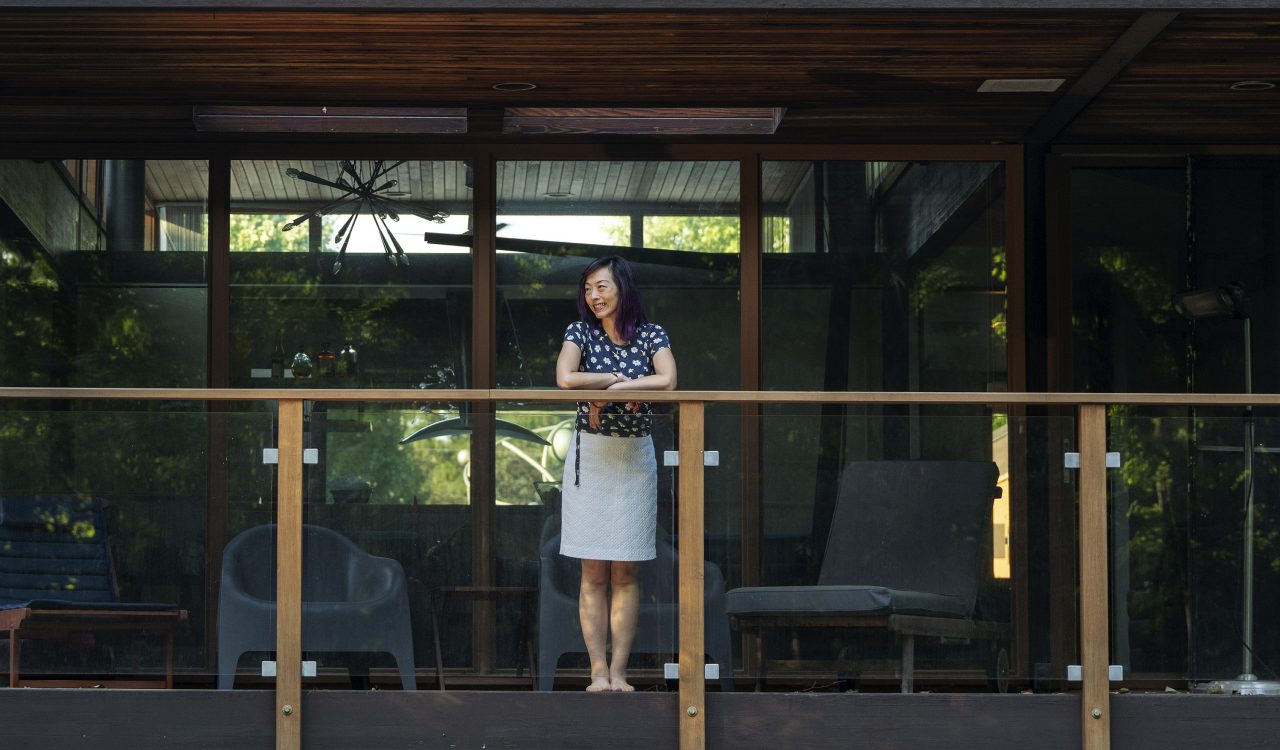 A woman stands on the second-floor balcony of a large home.