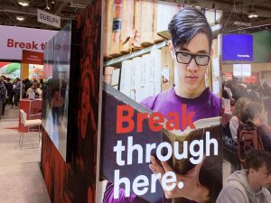 An advertisement on the side of a booth features a male student reading and reads 'Break through here.'