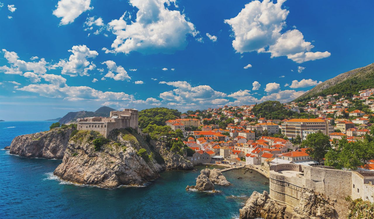 A coastal view of Croatia with many orange-roofed buildings under a sunny blue sky with white clouds.