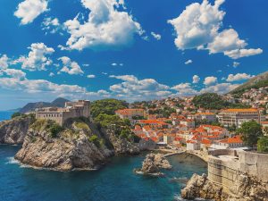 A coastal view of Croatia with many orange-roofed buildings under a sunny blue sky with white clouds.