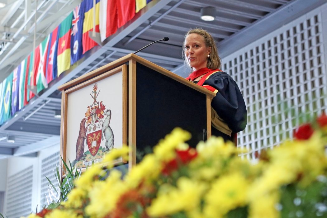 A woman in a graduation gown stands at a podium speaking.