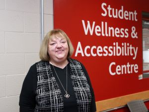 Dianne Jansen stands in front of a red wall with large white letters that read ‘Student Wellness and Accessibility Centre.’