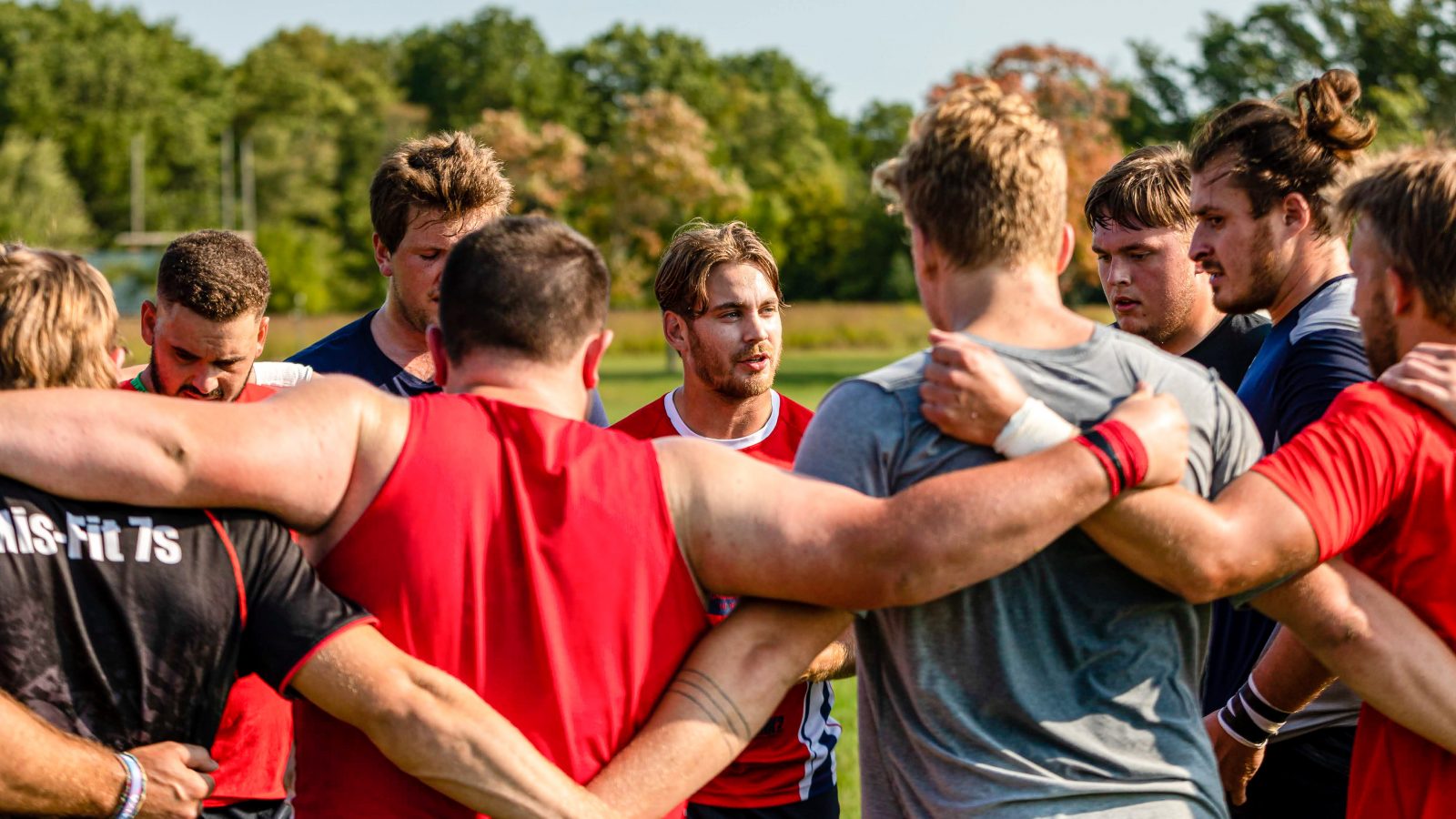 Athletes of a men’s rugby team lock arms in a huddle.