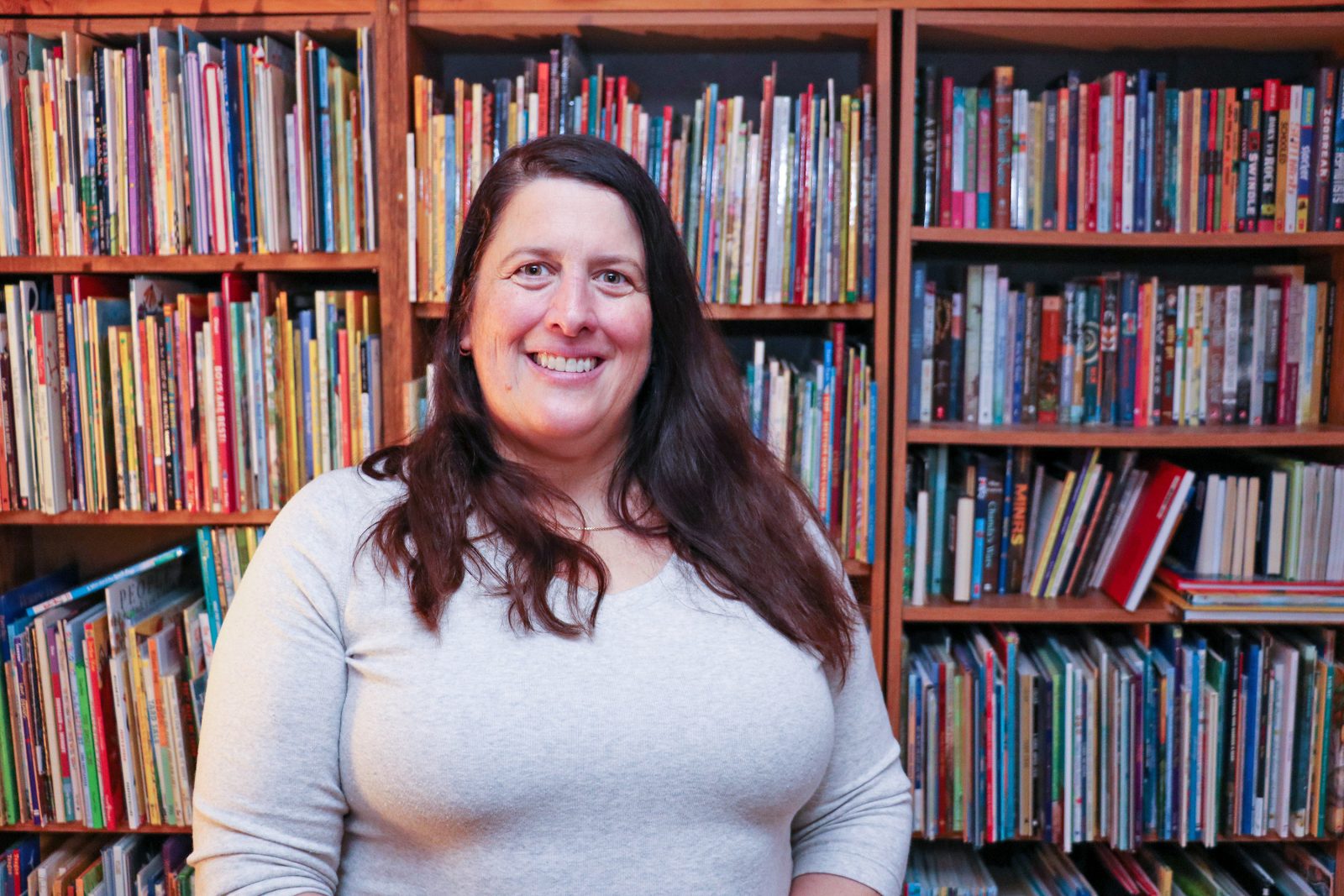 Brock University Professor Kari-Lynn Winters stands in front of several shelves filled with colourful children’s books.