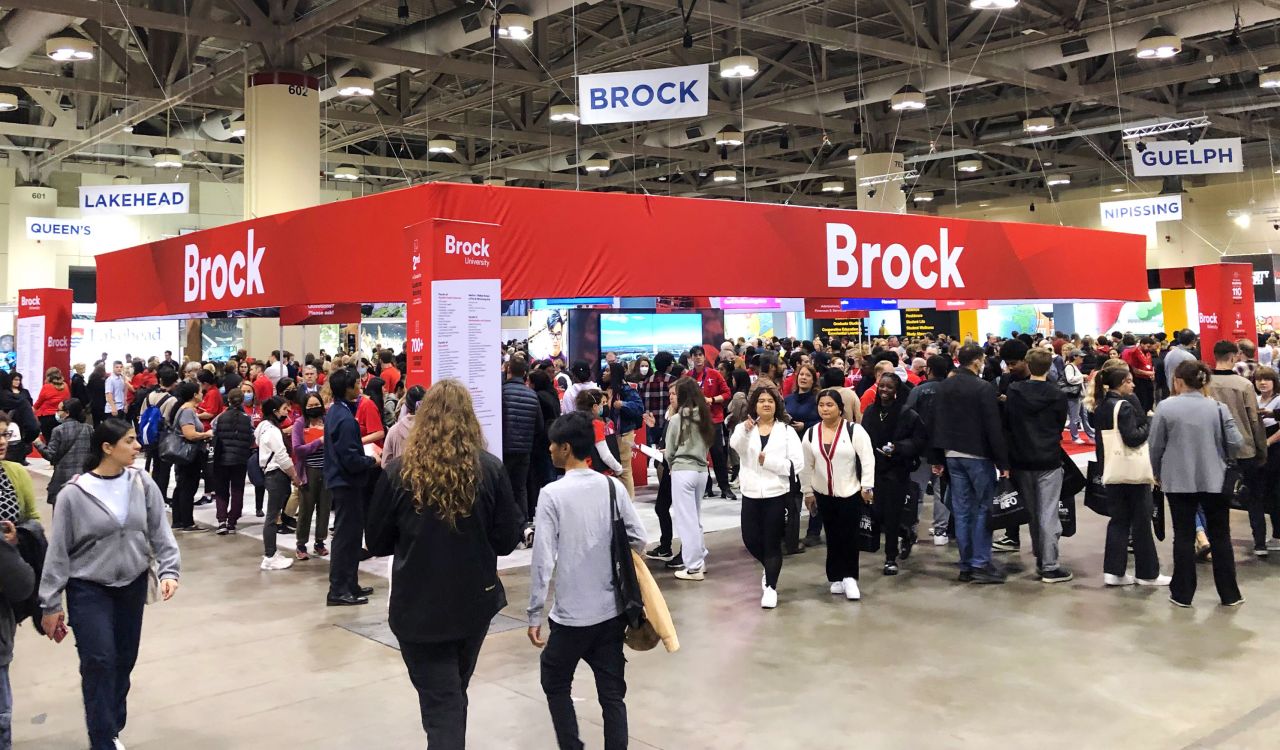Crowds of people walk in and around a Brock University display area.