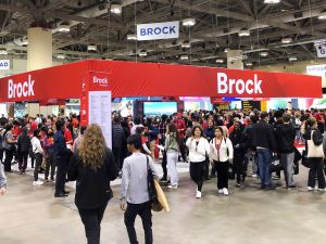 Crowds of people walk in and around a Brock University display area.