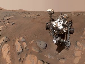 A wheeled space rover sits on the rocky red surface of Mars.