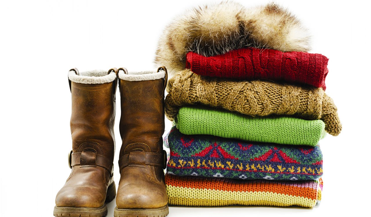 Winter boots, cap and stack of various sweaters isolated on white background