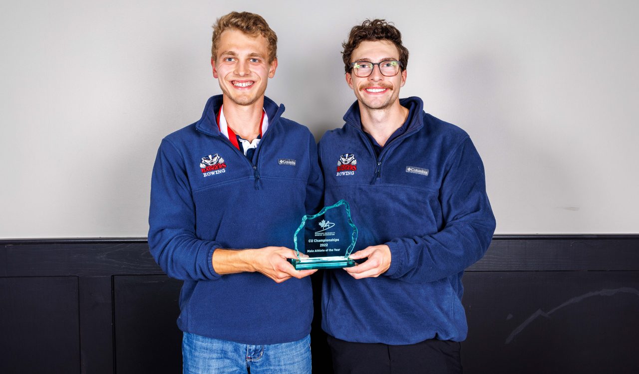 Two men stand holding an award between them.