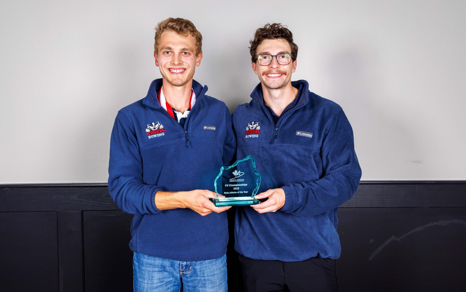 Two men stand holding an award between them.