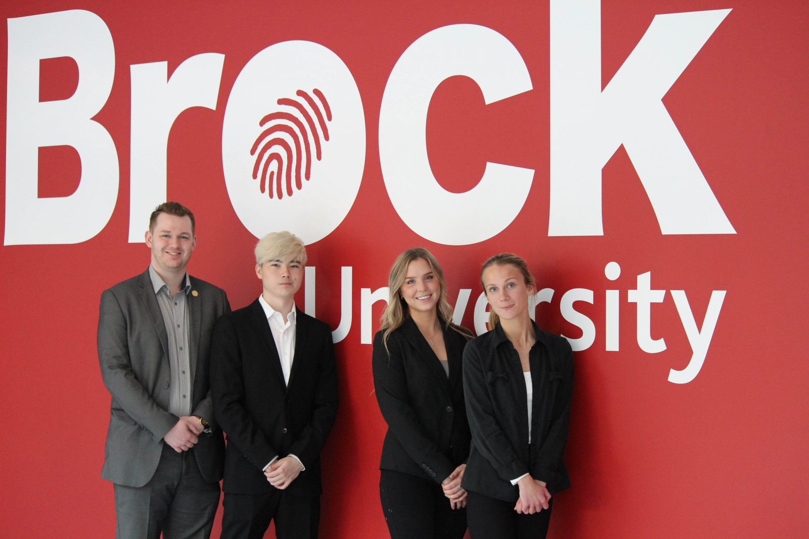 Four students stand in front of an oversized red Brock University sign