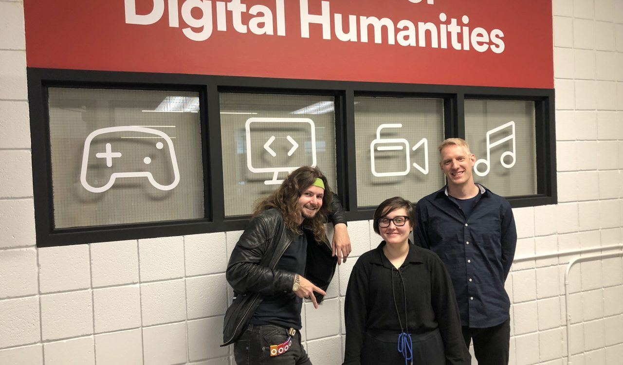 Three people stand in front of Brock’s Centre for Digital Humanities sign.