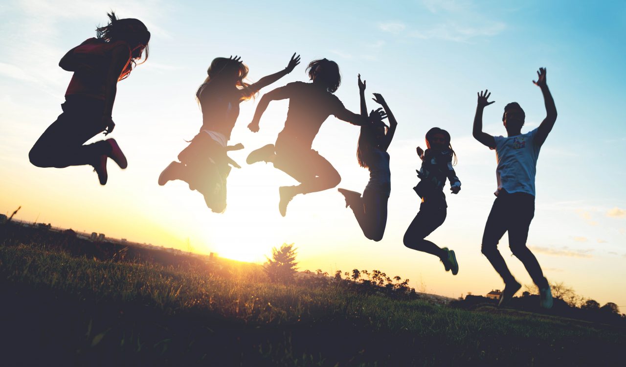 Silhouettes of six people jumping in the air against a sunset.