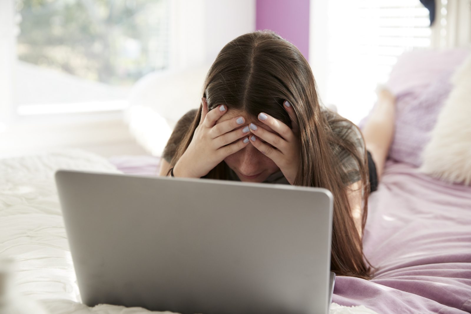 A girl sits with her head in her hands behind a laptop.