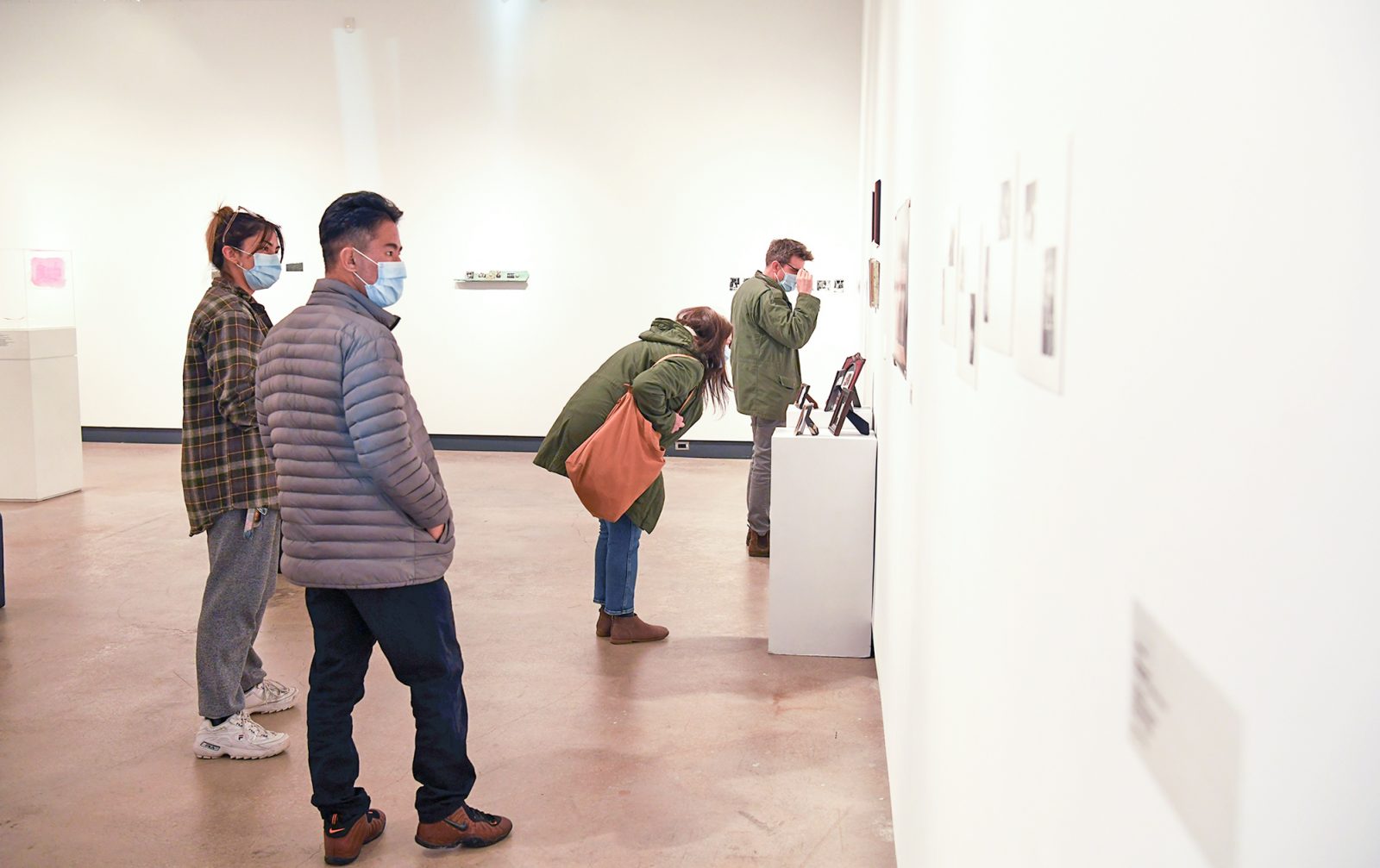 Four individuals in an open art gallery examining photographs put up on white walls.