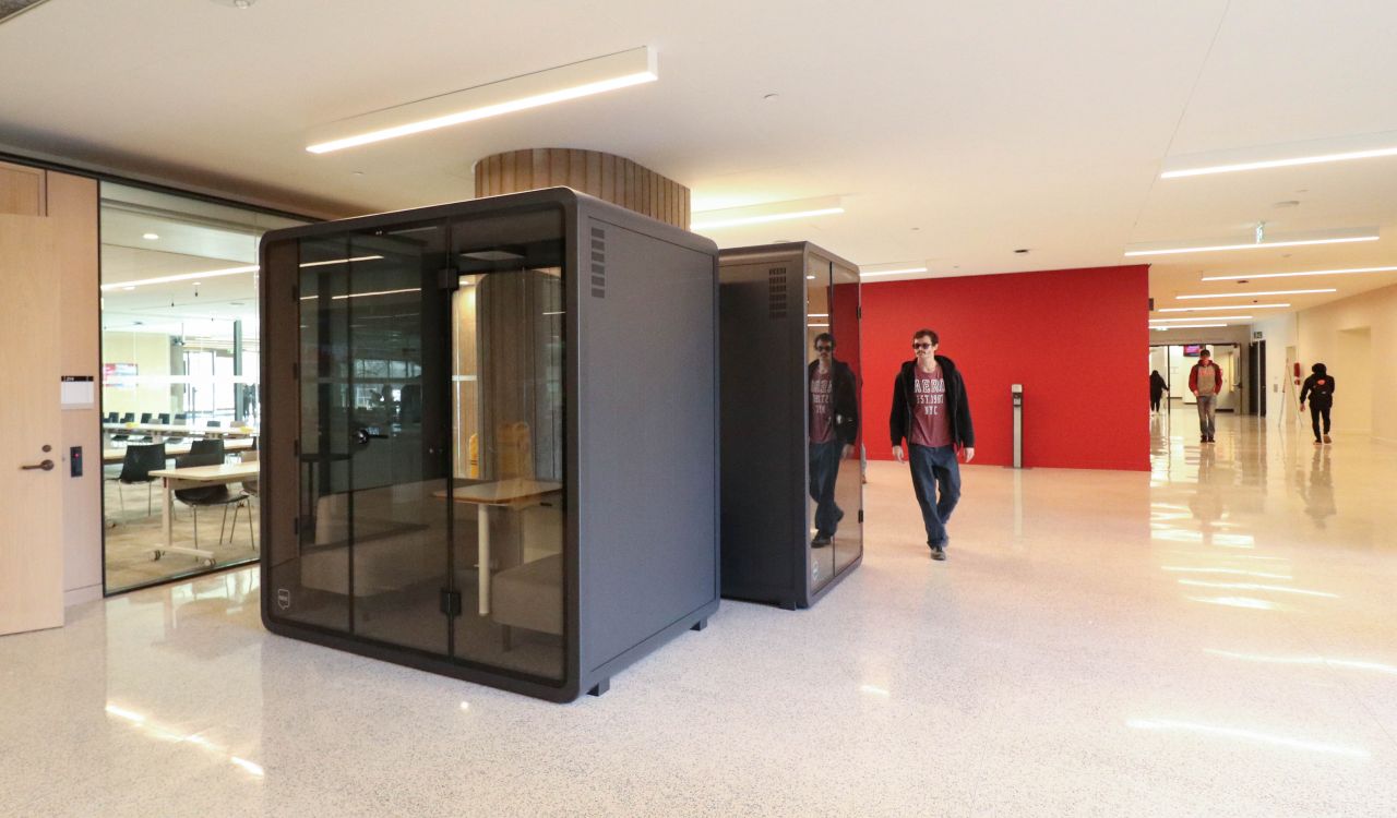 A booth for small meeting spaces in a hallway, with people walking by.