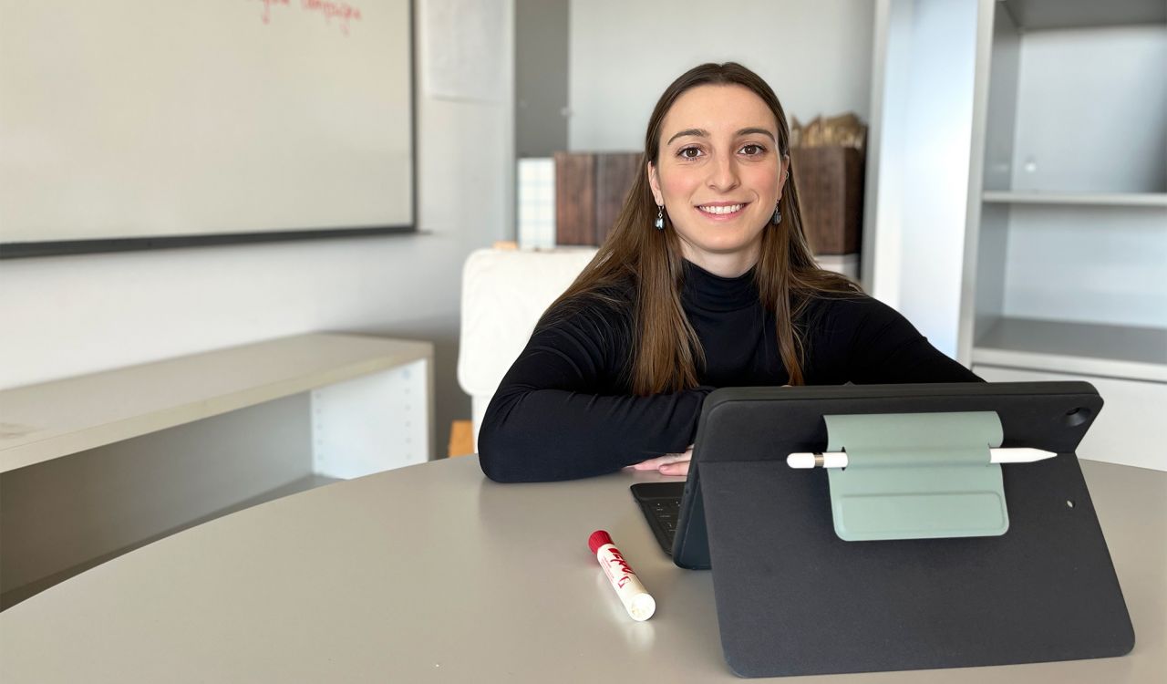 Tia Greto, Brock University Psychology master’s student, sits at a table with a tablet in front of her. A whiteboard with writing on it is behind her.