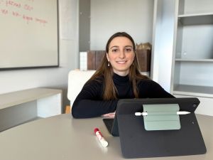 Tia Greto, Brock University Psychology master’s student, sits at a table with a tablet in front of her. A whiteboard with writing on it is behind her.