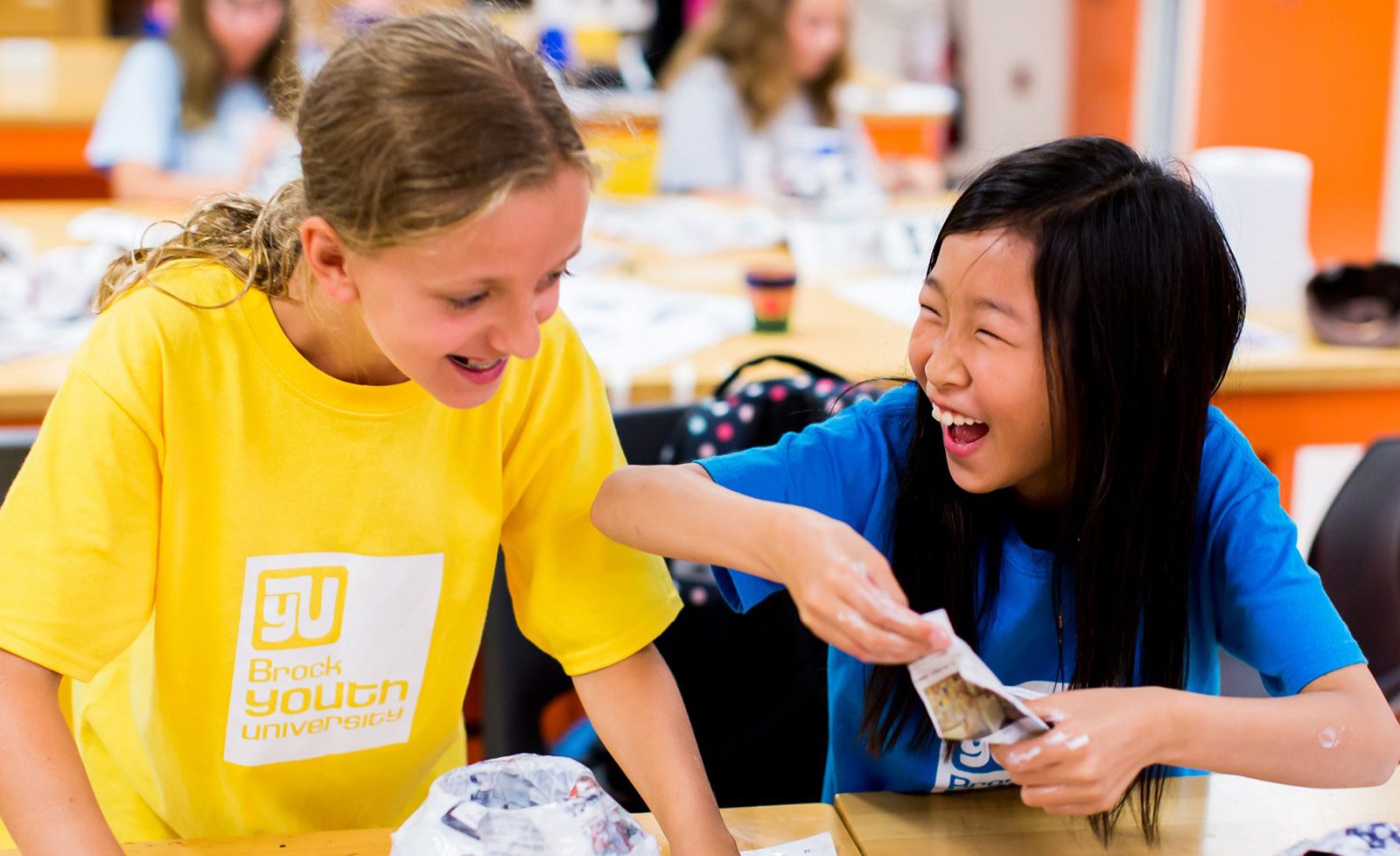 Two girls smile as they work on paper mache crafts.