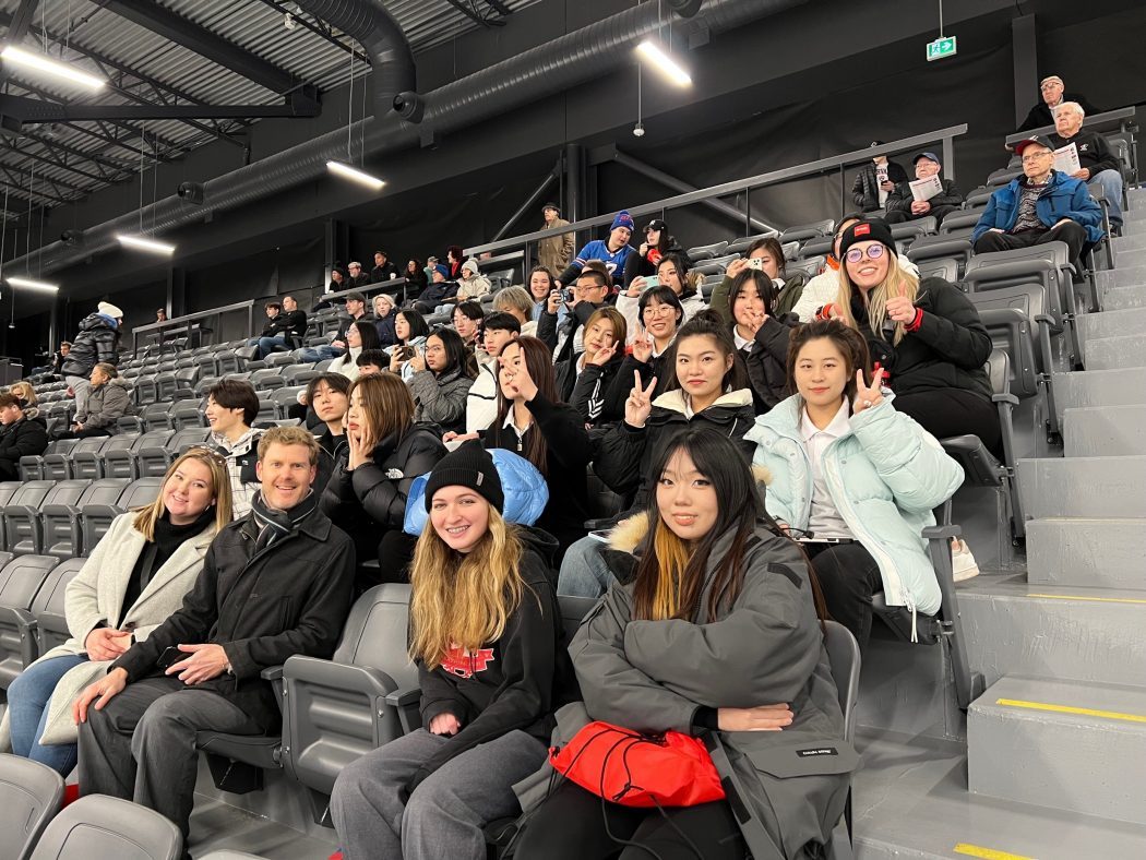A group of students sits in the stands of a hockey arena.