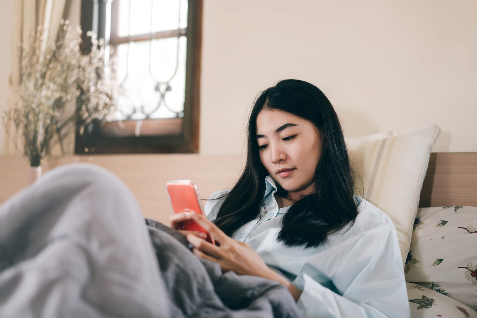 A woman sits on a bed while looking at her phone.