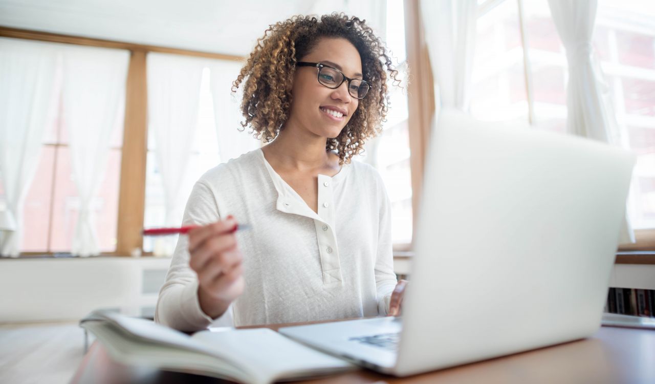 A woman looks at a laptop while holding a pen.