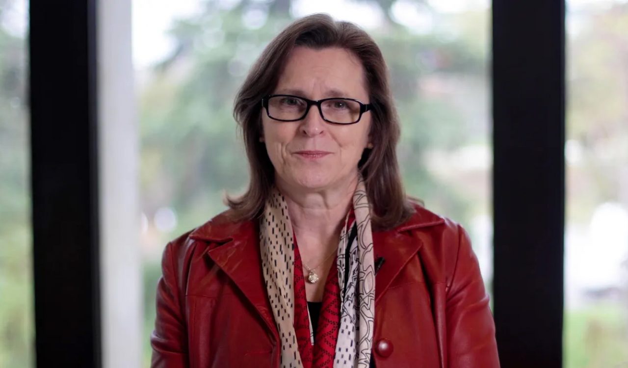 A woman in a red jacket sitting in front of a window.