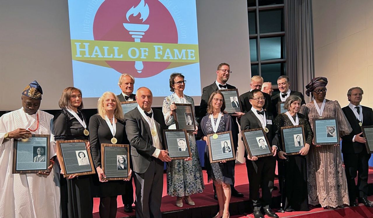 Two rows of people stand holding framed awards in front of a sign that says ‘Hall of Fame’