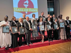 Two rows of people stand holding framed awards in front of a sign that says ‘Hall of Fame’
