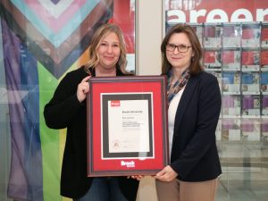 Two women stand next to each other holding a framed award.