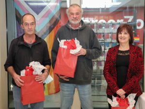 Two men and a woman stand next to each other, each holding a red gift bag.