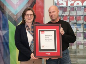 A woman and a man stand next to each other holding a framed award.