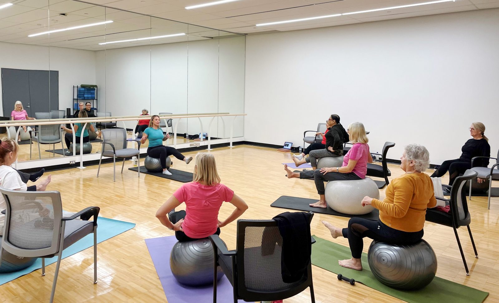 Bfit members participate in an exercise ball class led by a graduate student. Participants each sit on a yoga ball while watching the instructor.
