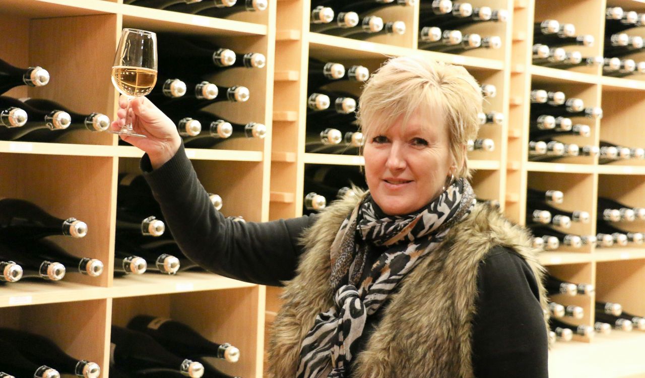 Woman in wine cellar raises a glass of white wine.