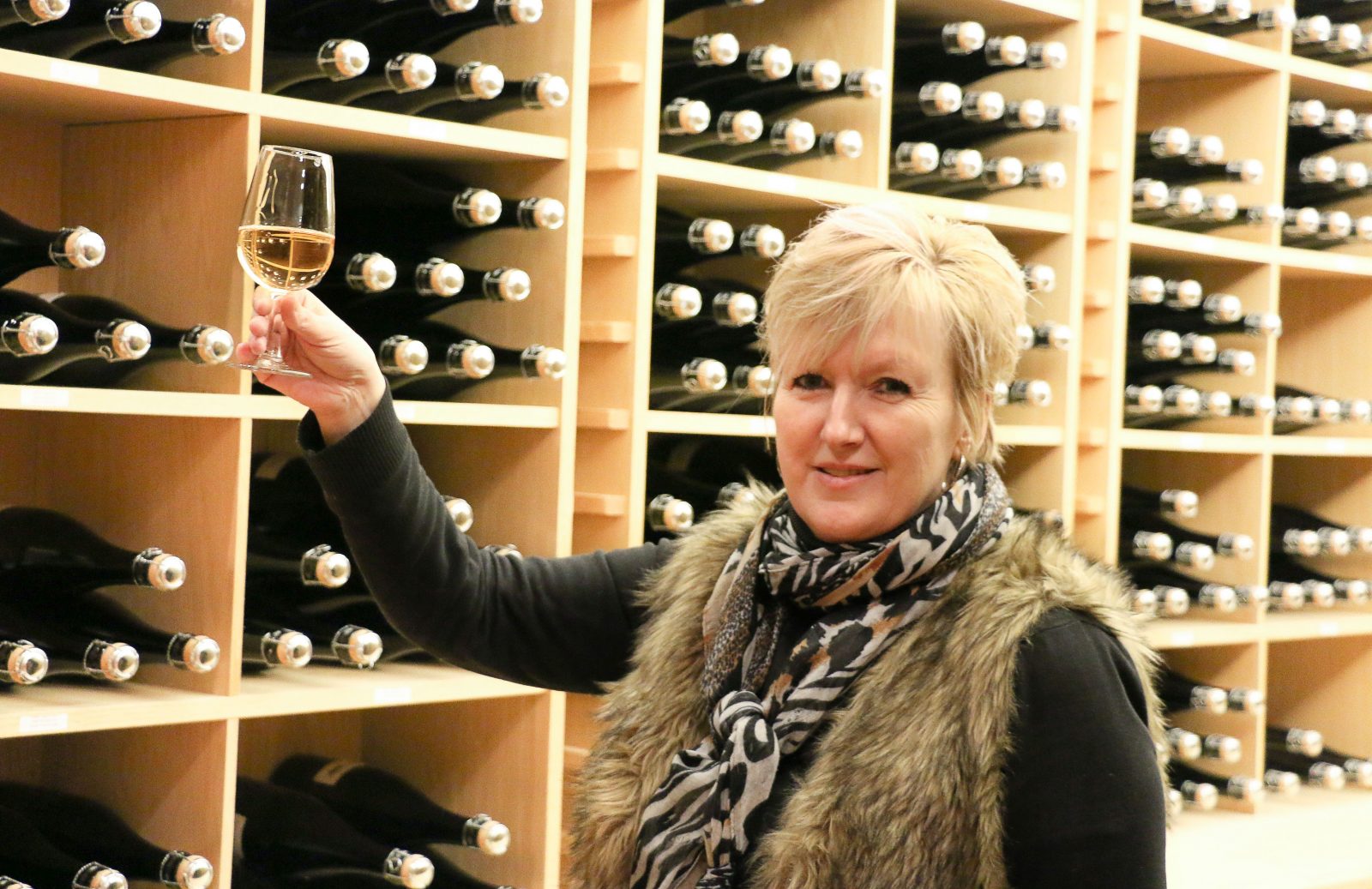 Woman in wine cellar raises a glass of white wine.