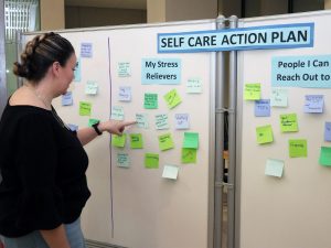 A woman looks at a white board containing many colourful sticky notes with suggestions for self-care.