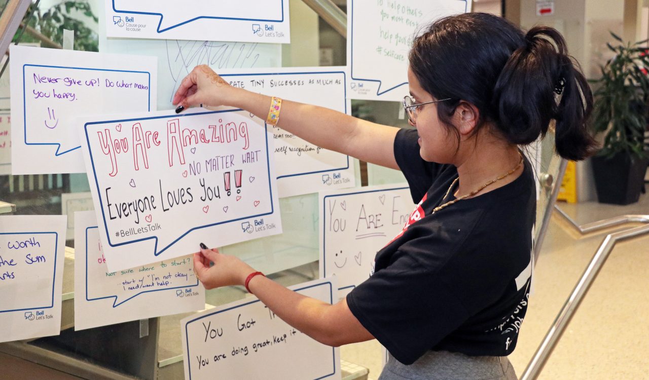 Second-year Psychology student Mishrka Bucha looks at the message she wrote in a conversation bubble before adhering it to the side of the stairs in Brock University's Market Hall. The sign reads 