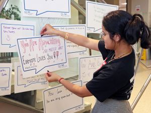 Second-year Psychology student Mishrka Bucha looks at the message she wrote in a conversation bubble before adhering it to the side of the stairs in Brock University's Market Hall. The sign reads "You are amazing not matter what. Everyone loves you!!"